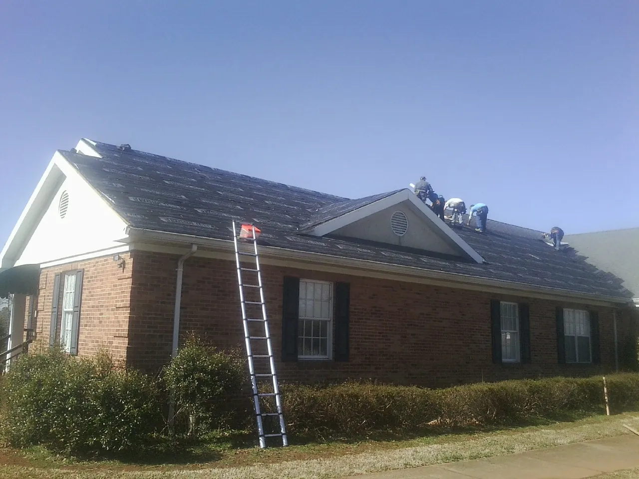 Crew tearing shingles off a brick ranch roof with a ladder set — Emergency Roof Repair work by our crew in Milford